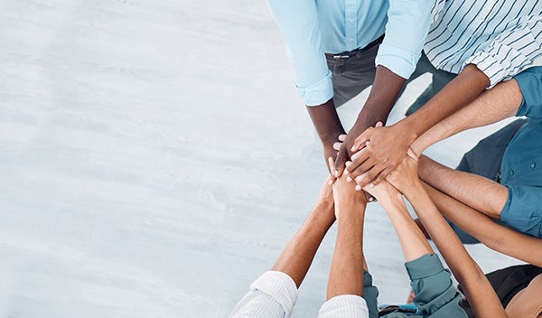 Happy employees with their hands in a huddle for go team